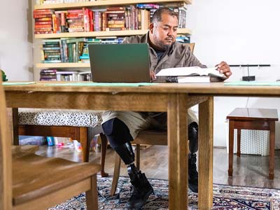 A man with prosthetic legs working on a laptop with books