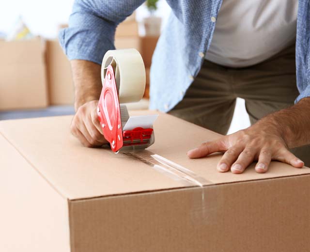 A person using packing tape to seal a cardboard box.