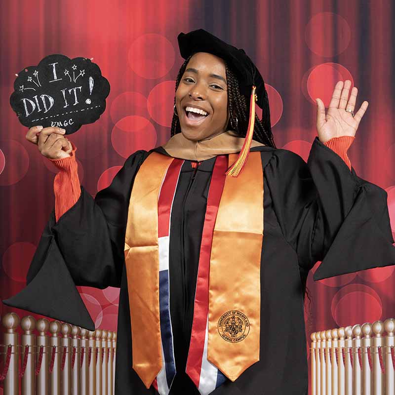 A UMGC graduate in graduation regalia holding a sign that says, "I did it!"