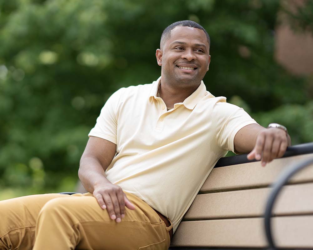 A UMGC graduate sitting on a bench outside smiling.