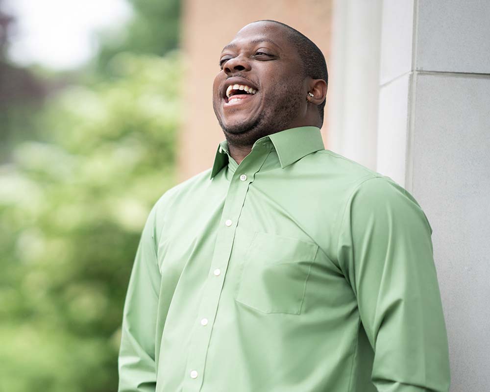 A UMGC graduate in professional clothing laughing in an outdoor location.