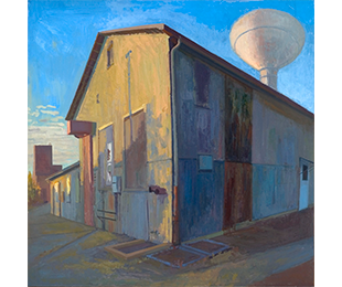 A tan building partly in shadow, its windows boarded up, with smaller structures and a water tower behind it.