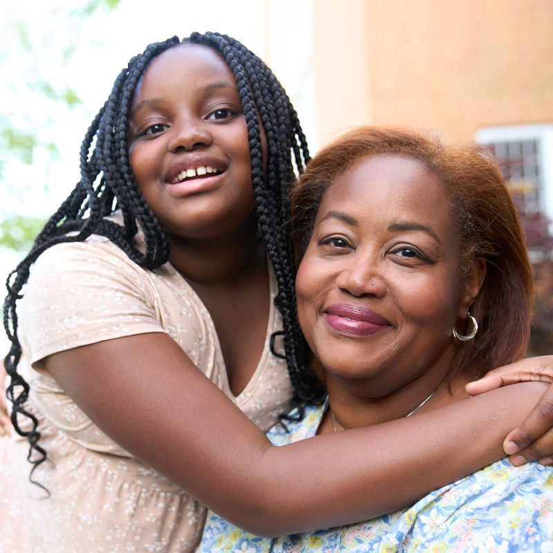 A young adult and an adult looking at the camera and smiling.