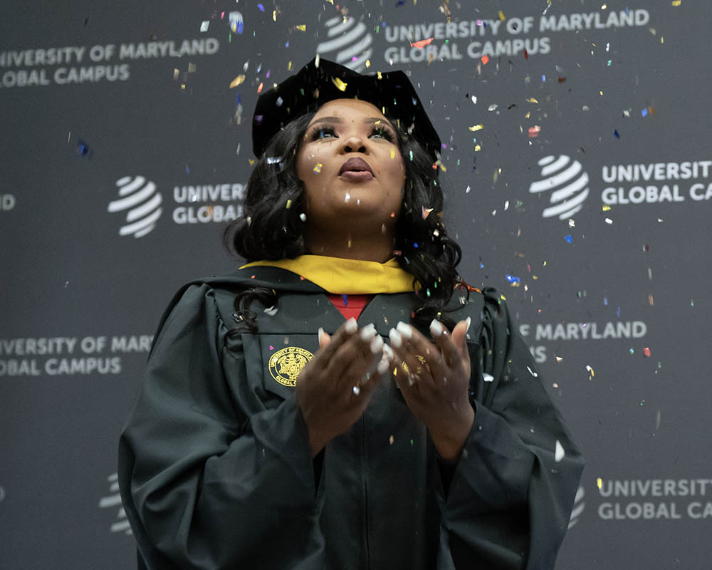 A UMGC alum in graduation regalia celebrating with confetti.