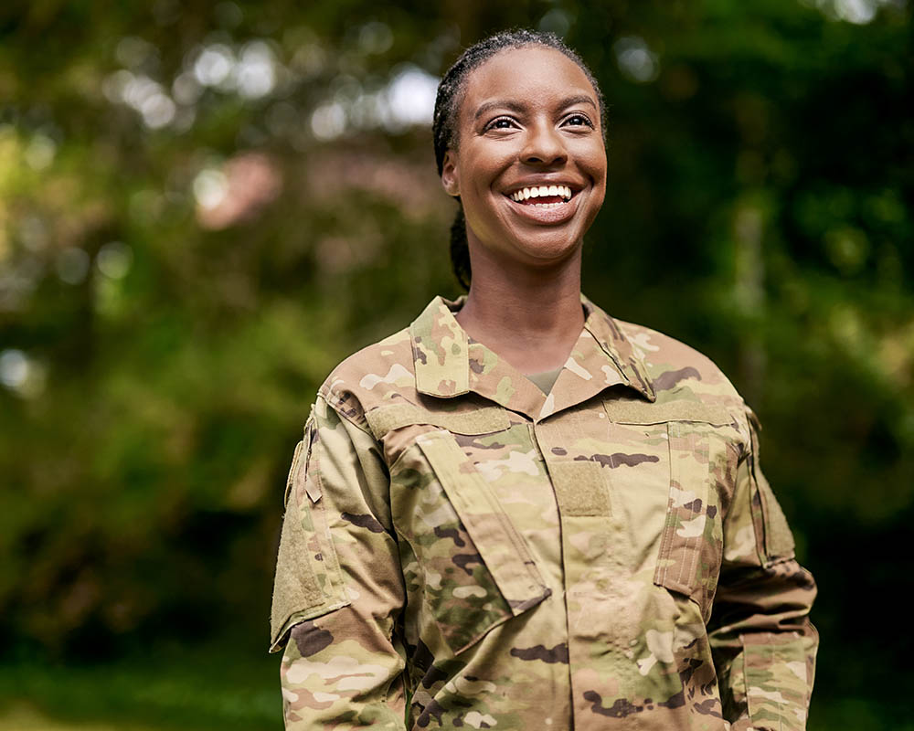 A woman in a military uniform smiles and laughs, looking at something behind the camera.