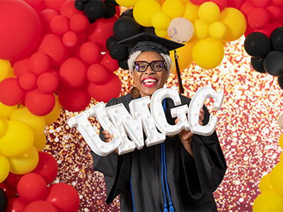 A UMGC graduate holding a UMGC sign and smiling.