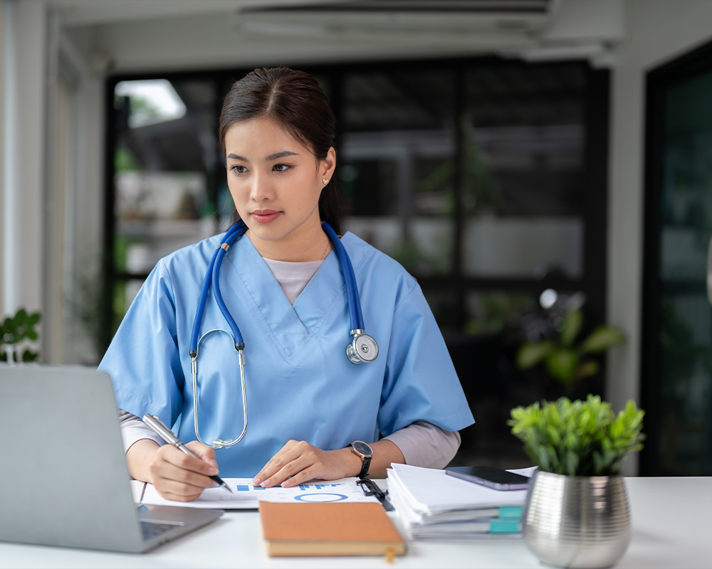 A medical professional looking at a laptop and taking notes.
