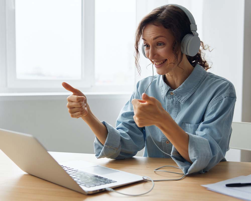 A person giving a thumbs up sign while looking a their laptop.