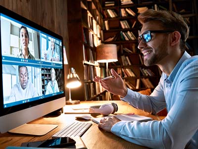 A person looking at a computer monitor with a group video call on the screen.