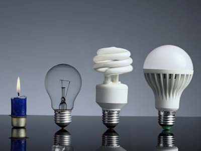 A candle and three light bulbs in a row depicting the evolution of light technology.