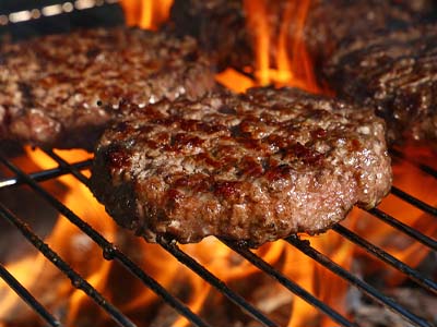 Hamburgers on the grates of a grill with flames.