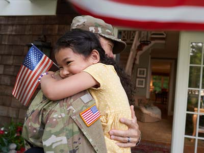A child holding an American flag hugging a person in uniform.