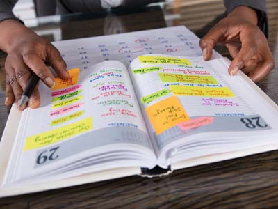 A person holding a daily planner that has colorful post-its and notes written on it.