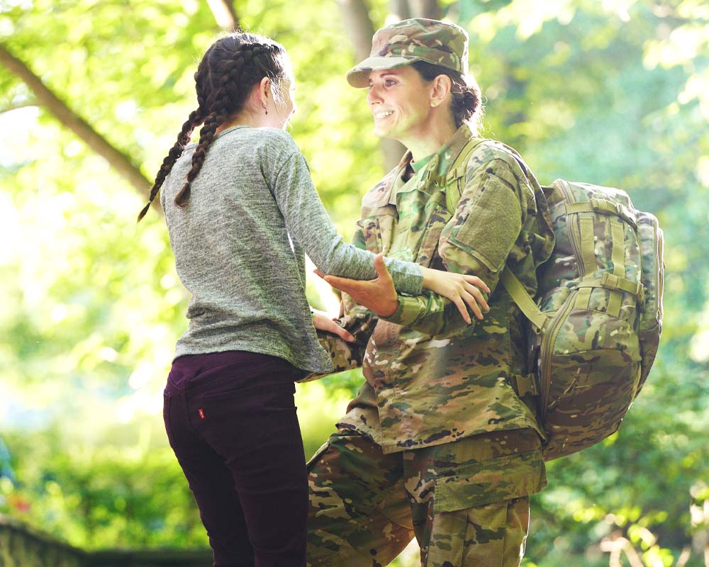 A person in a military uniform greeting another person outside and smiling.