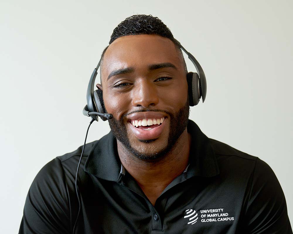 A person in a University of Maryland Global Campus shirt wearing a headset.