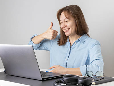 A person using a laptop and giving the thumbs up sign.