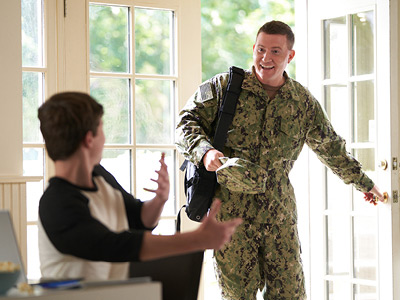 A person in a military uniform opening a door to another person sitting who looks surprised.