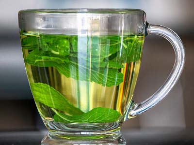 A clear mug of tea with peppermint leaves.
