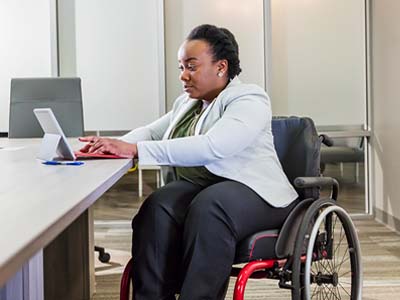 A person in a wheelchair sitting at a table and typing on a tablet.