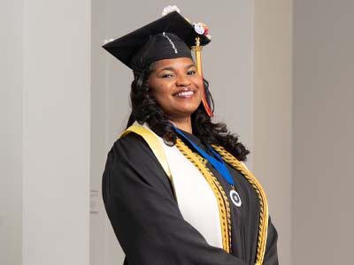 A person in a graduation cap and gown smiling.