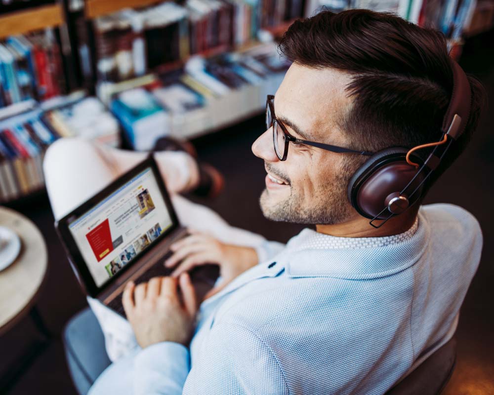 A man wearing headphones types on a laptop which shows the UMGC homepage.