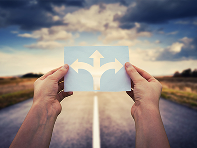 A person holding a piece of paper with multiple turn arrows in front of an open road.