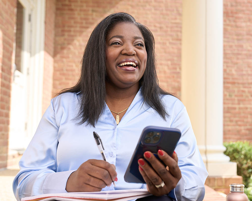 A person smiling while holding a pen and a cell phone.