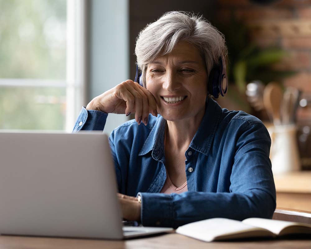 A person wearing headphones, smiling, and working on a laptop.