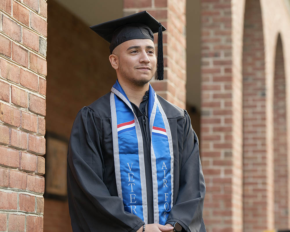 A UMGC graduate standing in graduation regalia.
