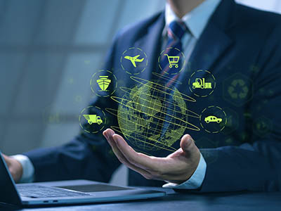 An abstract image of a person using a laptop and holding a globe surrounded by transportation-related icons.