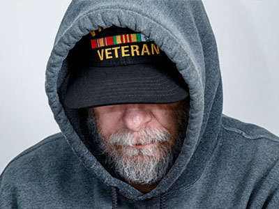 A person in a hoodie wearing a hat that says "Veteran" on it.