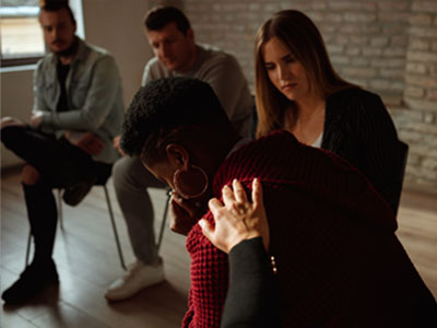 A person grieving while other people surround them in a seated circle.