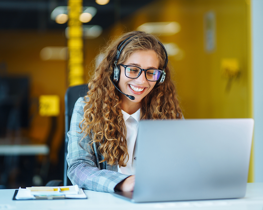 Person with headset smiling while typing on a laptop.