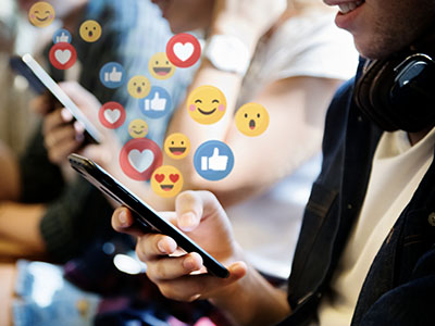 A person using a mobile phone with various emojis appearing to float up from the phone.