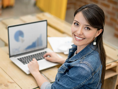 A person smiling for the camera and typing on a laptop.
