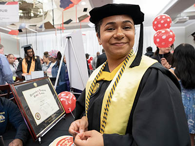 A UMGC graduate in graduation regalia smiling.