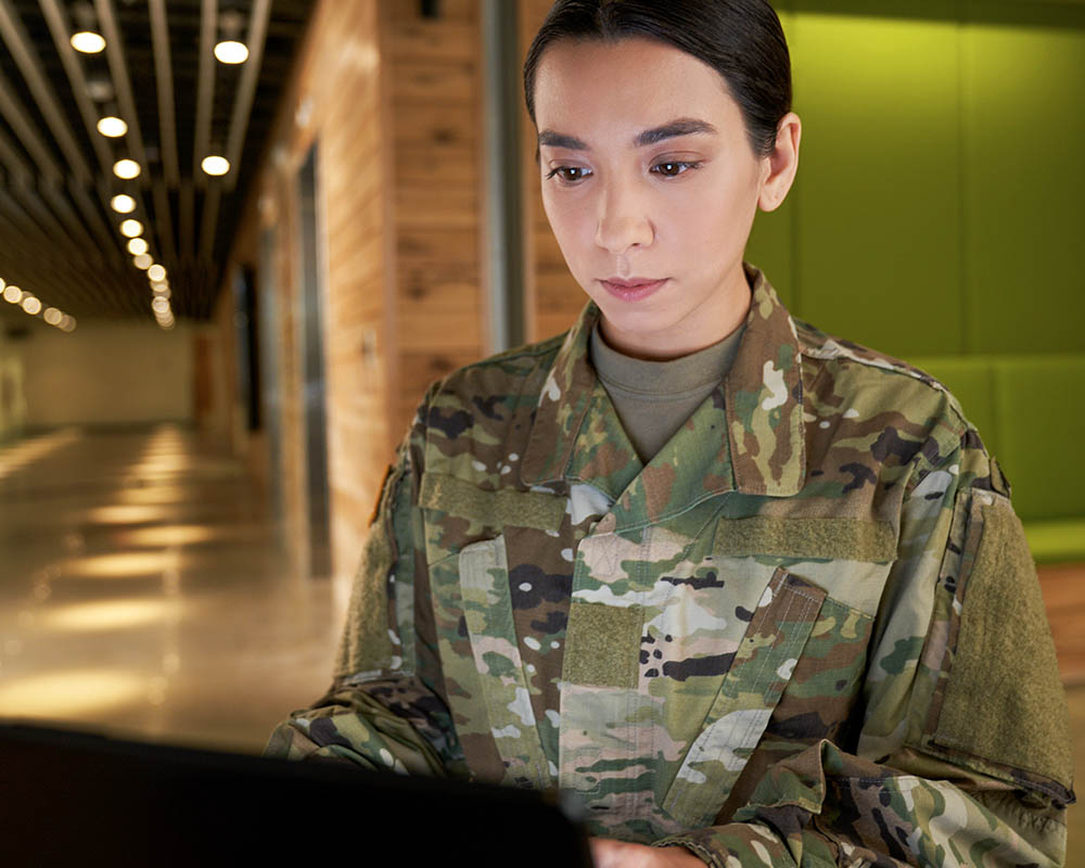 A person in a military uniform looking at a laptop.