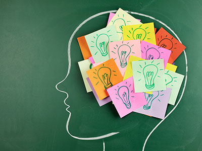 Multiple sticky notes with light bulbs drawn on them placed on a chalk drawing of a person's head.