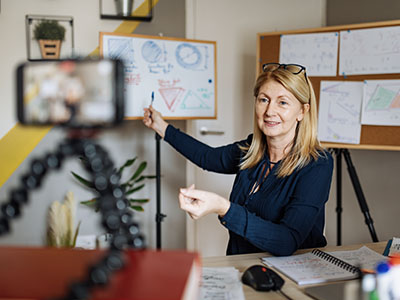 A mobile phone placed on a tripod capturing a person using a whiteboard.