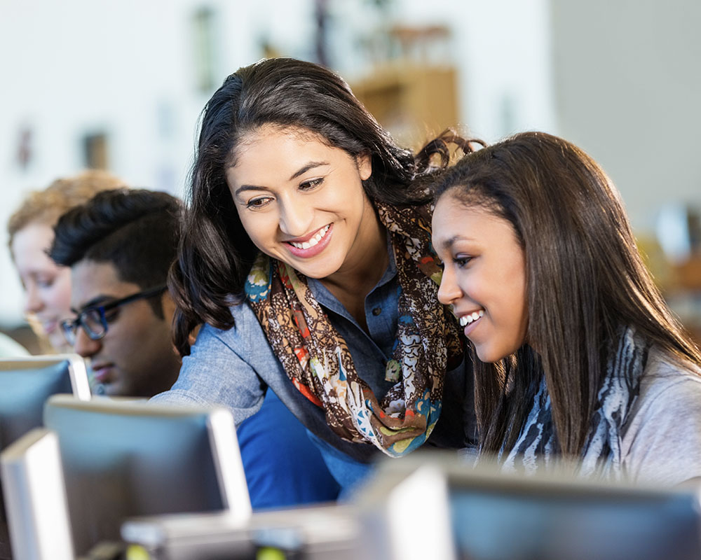 Two people in a classroom looking at a computer screen and smiling.