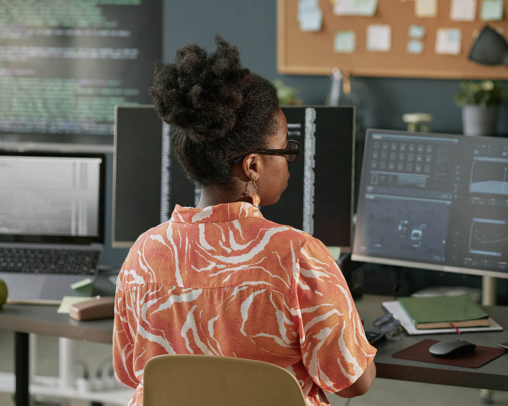 A person looking at several computer monitors showing charts and code.