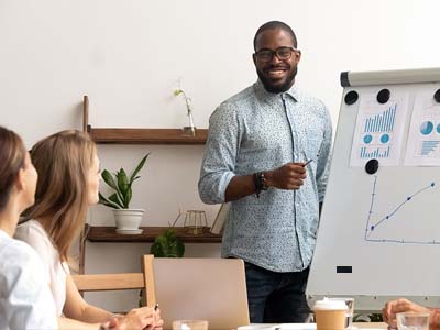 A person smiling while giving a presentation on a whiteboard.