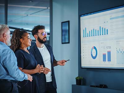 Three people looking at a large screen with various graphs and charts shown.