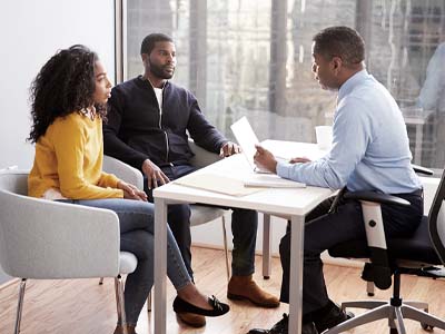 A person at a desk talking to two people on the other side of the desk.