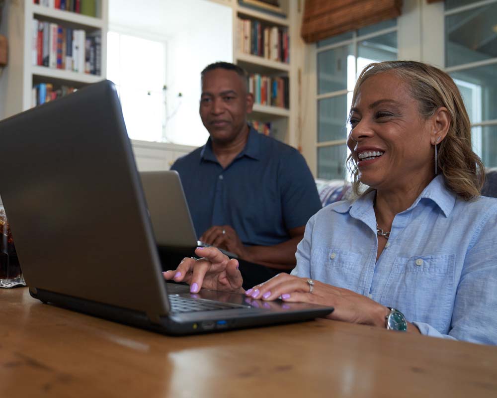 UMGC graduates, Michael and Leslie E., working on laptops.