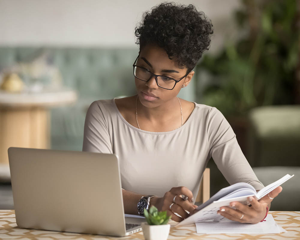 A person holding a book and looking at a laptop.