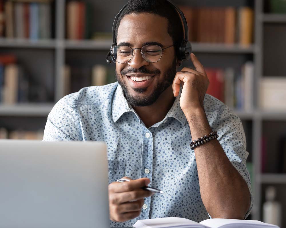A person smiling and wearing a headset while working on a laptop.