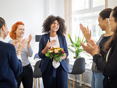 Woman standing and holding bouquet acknowledging the applause of the four other women standing around her.