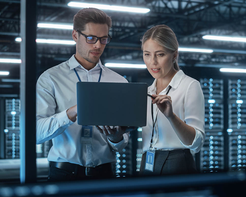 Two people standing and looking at a laptop.