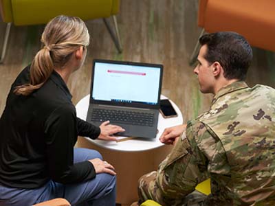 Two people, one in a military uniform, sitting and looking at a computer screen.